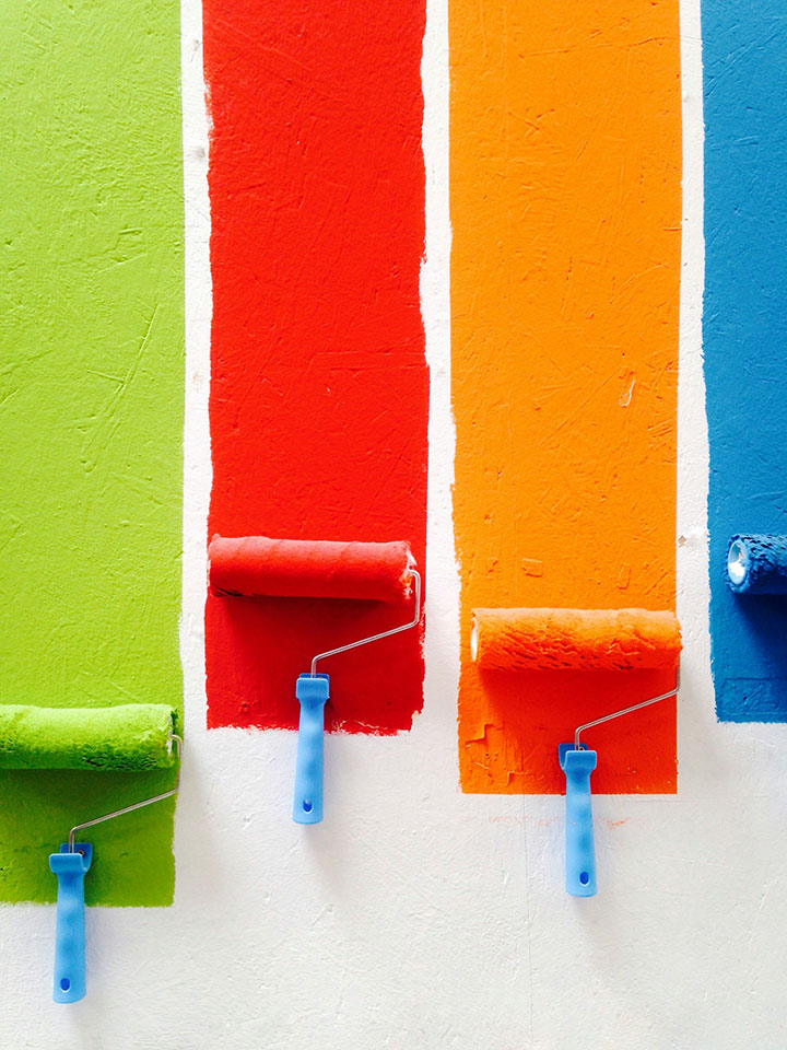 Four paint rollers and paint lines in green, red, orange, and blue