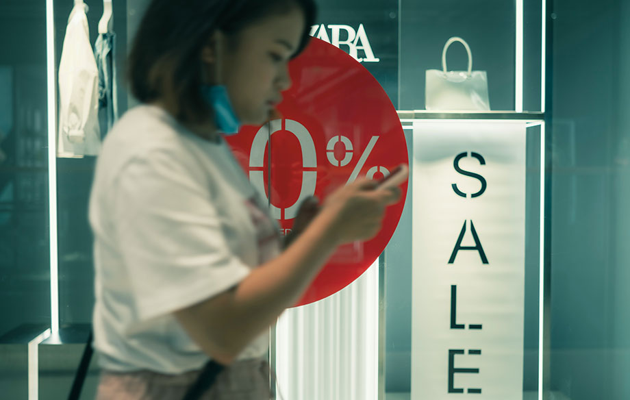 a woman walks past a store window that is advertising a sale
