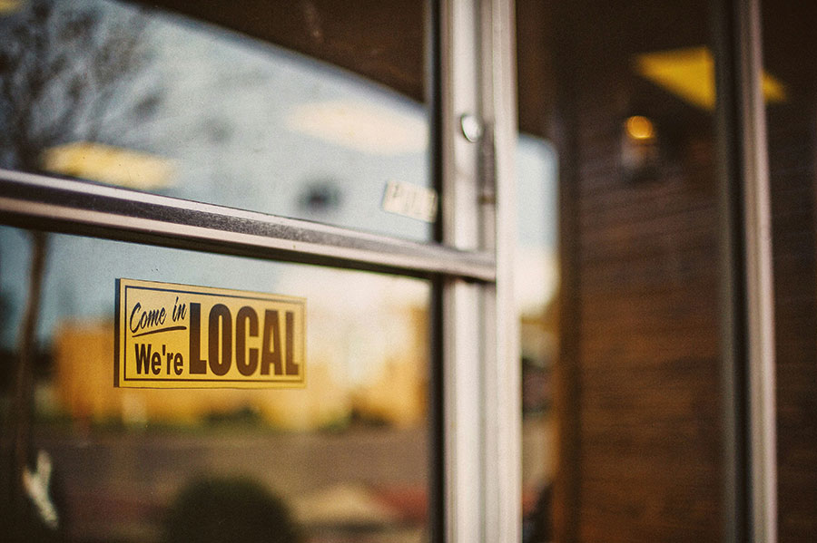 Storefront window with sign that says "Come in, we're local"