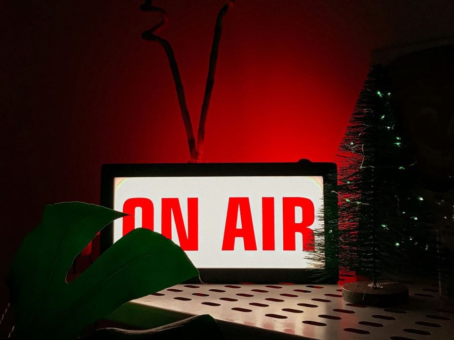 A mockup television displaying the words “ON AIR,” with a Christmas tree beside it on a red background.