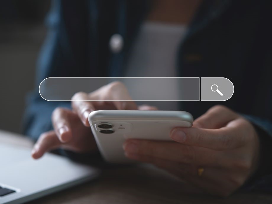 Close up shot of hands typing on a mobile phone with an interface of a search bar on the foreground.