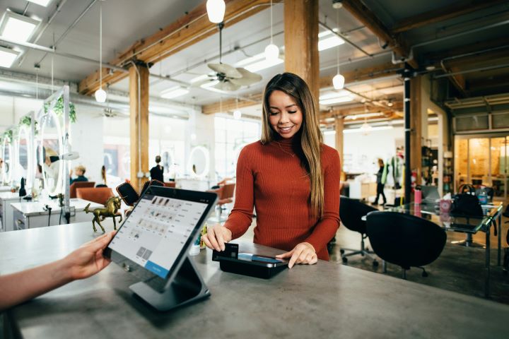a happy customer swipes her card to pay at the counter of a store