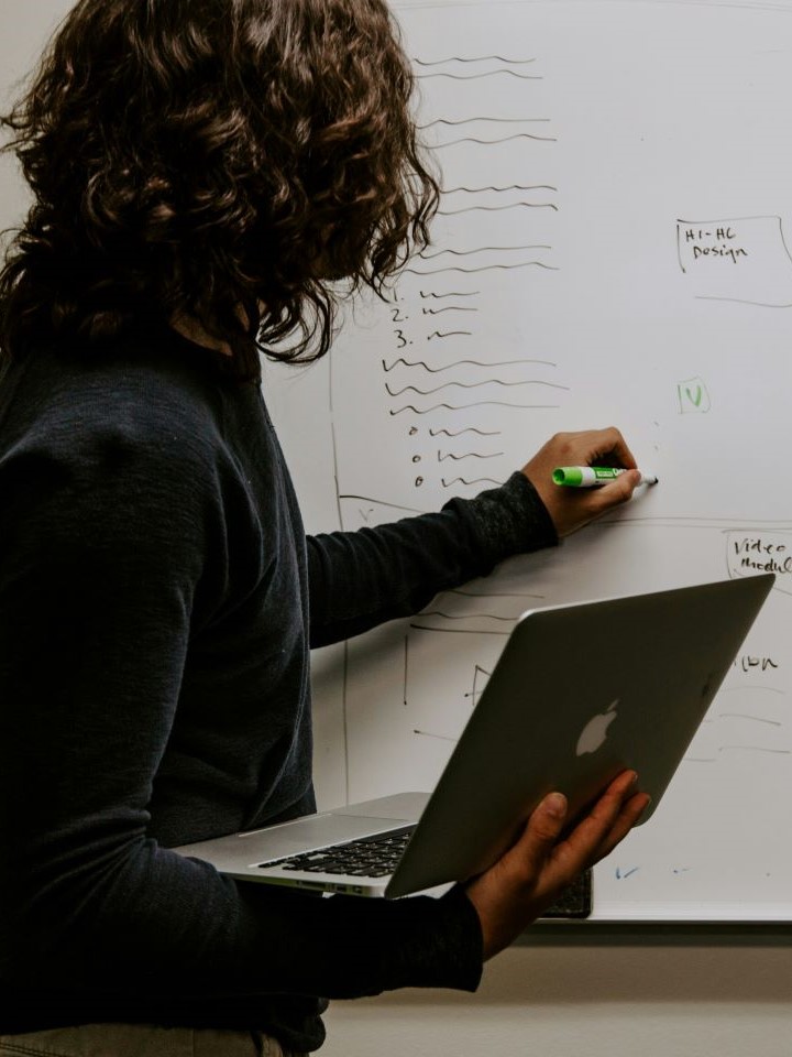 a man holding a laptop writes on a whiteboard