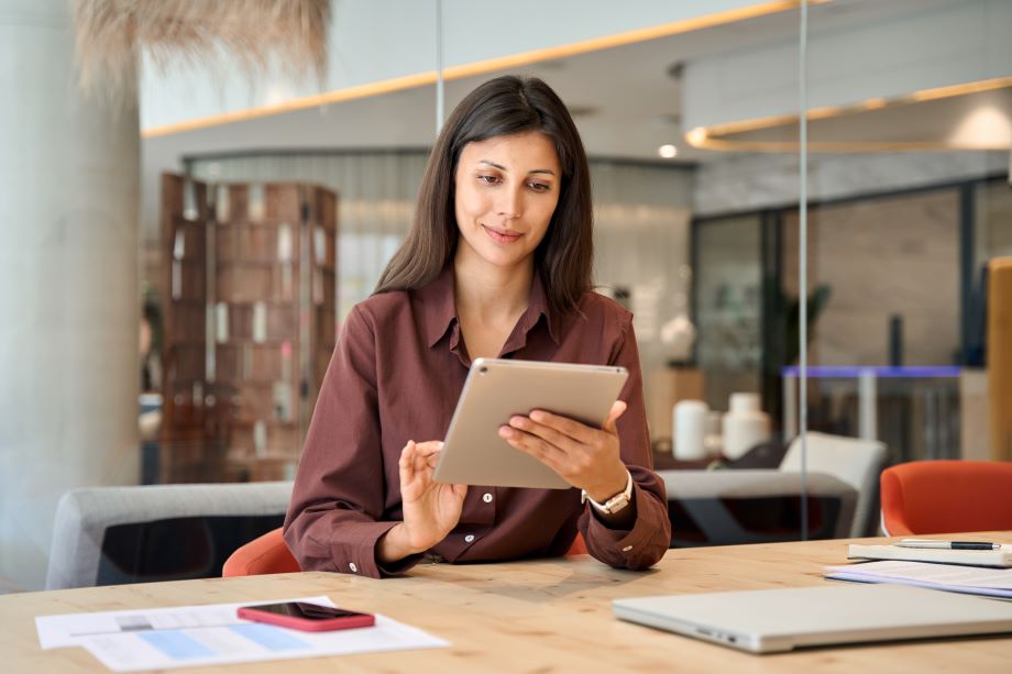 Business owner in a modern office space using a tablet computer and other devices on a large desk