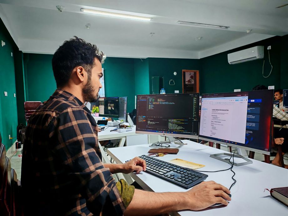 A developer working on dual monitors with code and a project plan document open, representing the technical SEO work behind AI-ready product data.
