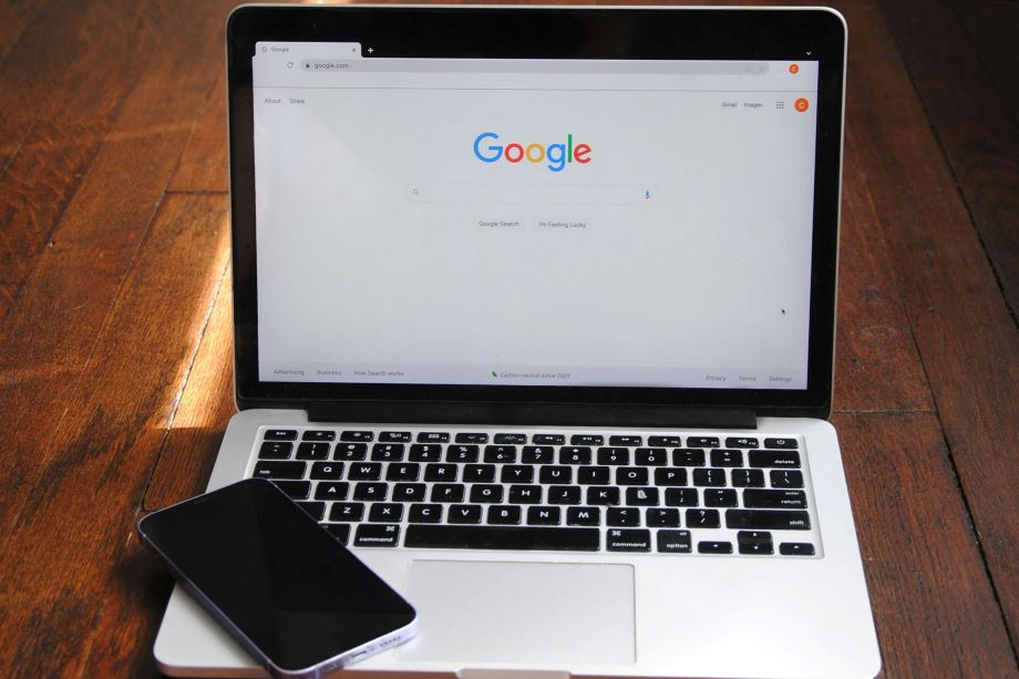 The Google search homepage open on a laptop with a smartphone resting on the keyboard.