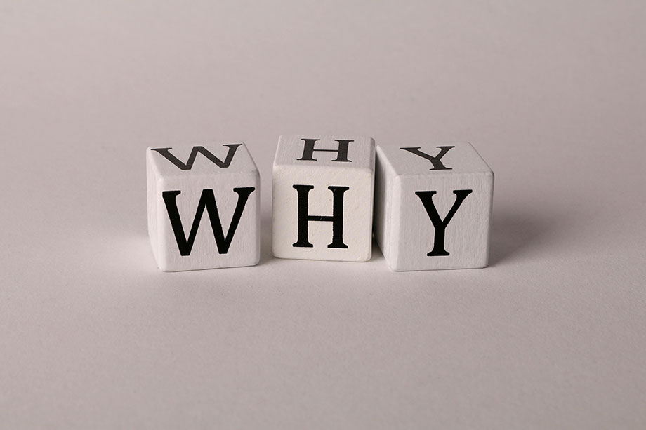 wooden-cubes-why-920 Three white wooden blocks sitting on a gray surface with black serif text spelling out the word why.