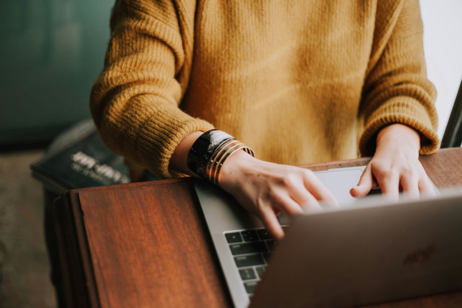 a close-up of a woman’s sweater and arms as she uses her laptop to launch an email marketing campaign.